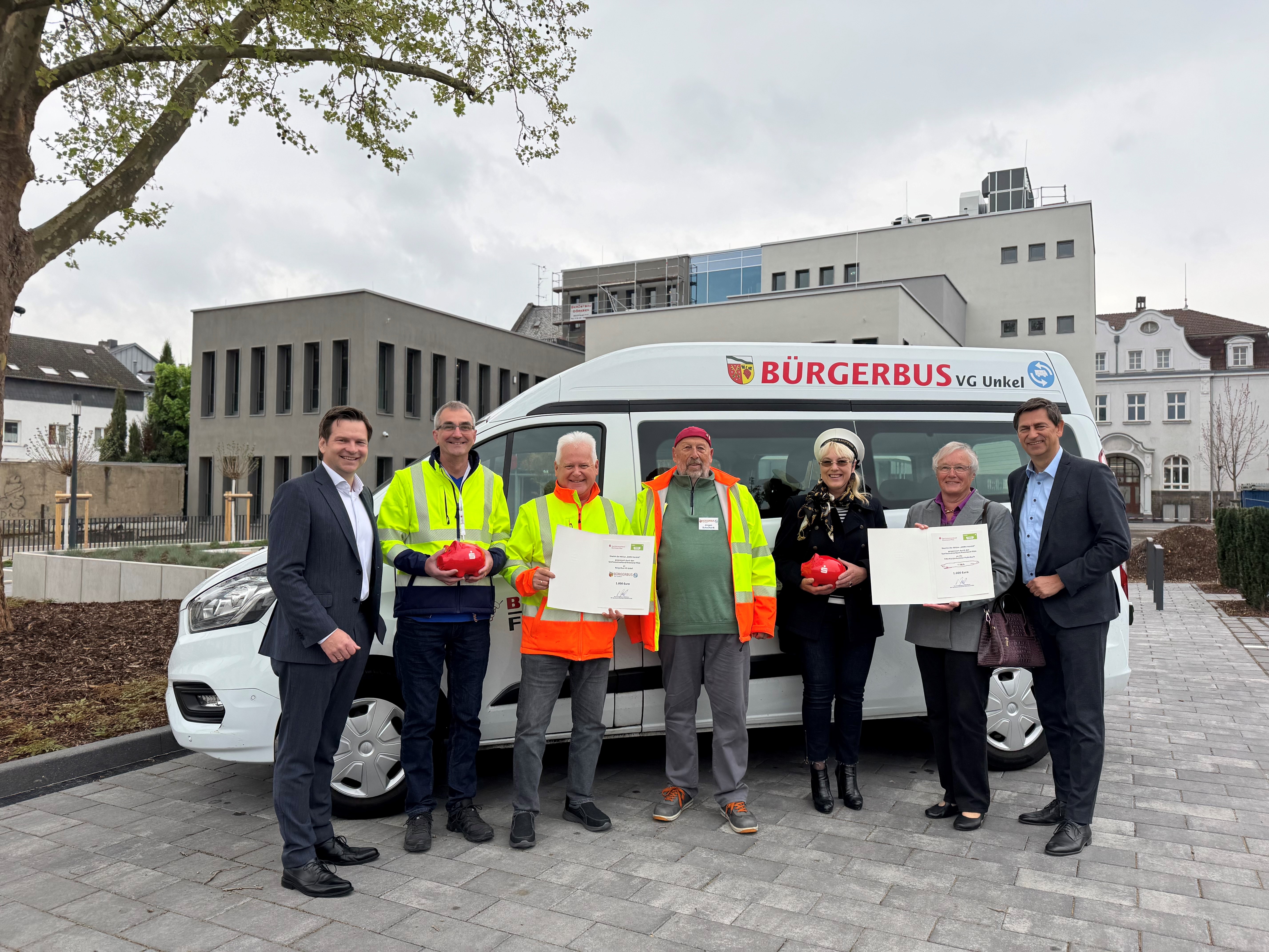 Gruppenfoto mit zwei Damen und fünf Herren vor einem Kleinbus, SVRP-Geschäftsführer Herr Roman Frank bei der Preisübergabe Gewinnspiel SWR4-vereint an den Verein Kleiderkammer Puderbach und den Bürgerbus VG Unkel in Neuwied