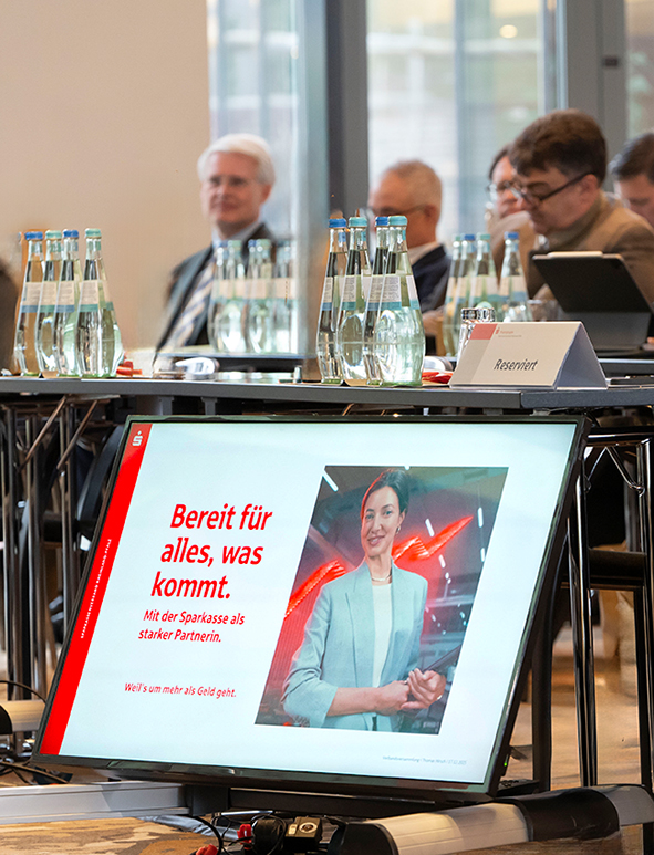 Blick auf Zuhörer einer Präsentation, im Vordergrund ein Bildschirm mit dem aktuell gezeigten Slider