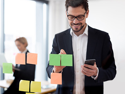 Mann beschriftet Post-it an einer Glasscheibe