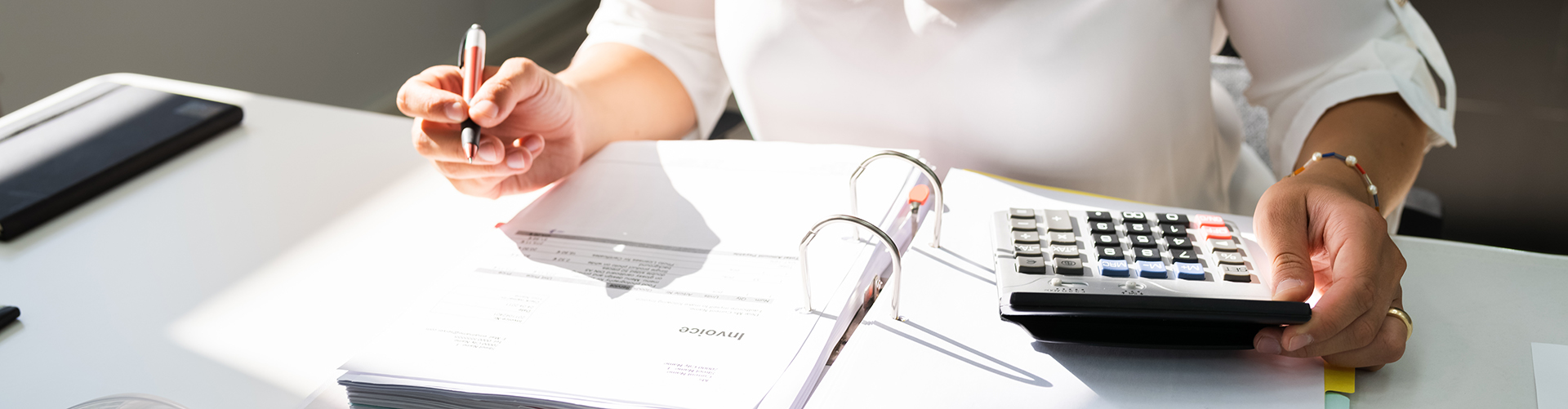 Hände einer am Schreibtisch arbeitenden Frau mit Stift und Taschenrechner
