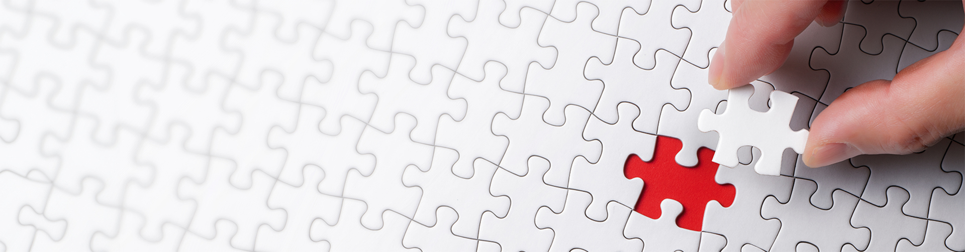 eine Person hält das letzte fehlende Puzzleteil über einem glatt weißen Puzzle