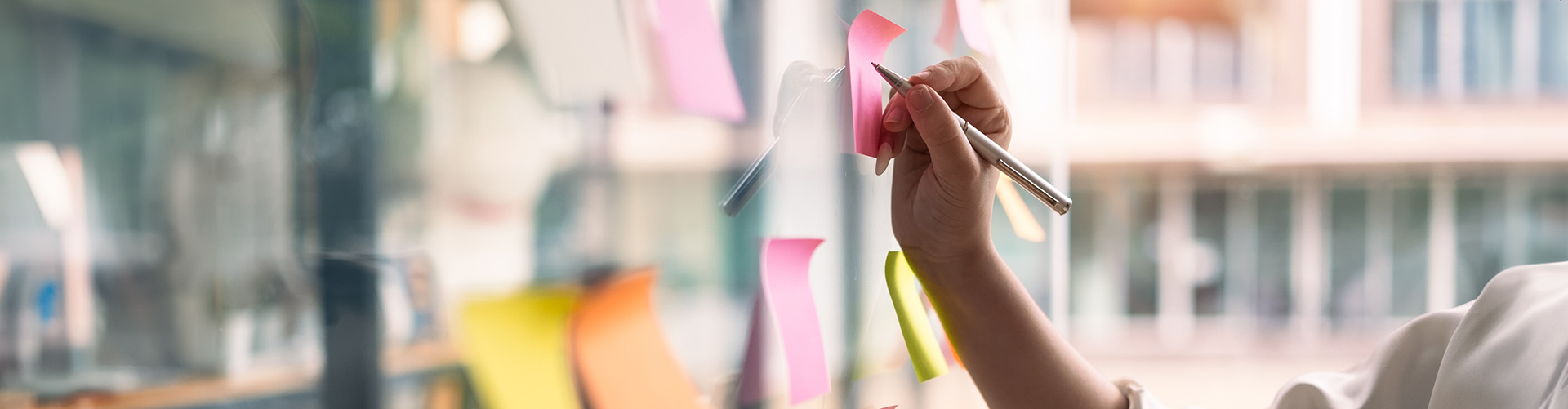 Hand schreibt auf Post its an Glasscheibe