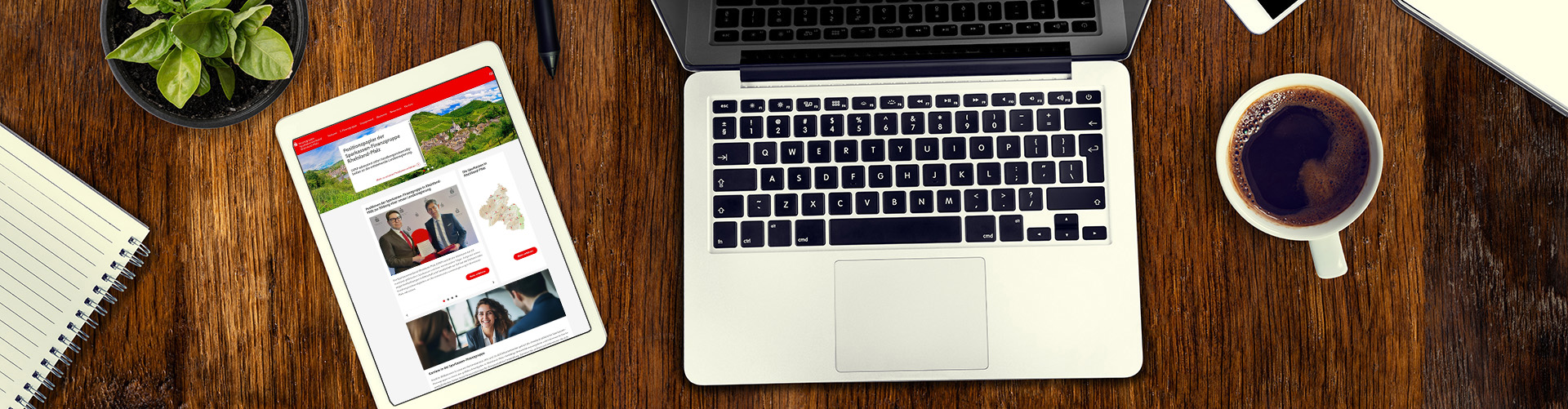 Blick von oben auf einen Schreibtisch mit einem Tablet, einem Notebook und einer Kaffeetasse