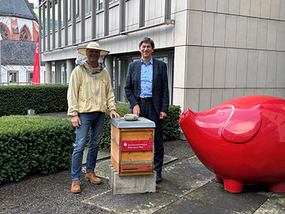 ein Imker steht mit dem Geschäftsführer des Sparkassenverbandes Rheinland-Pfalz, Herrn Roman Frank, hinter einem Bienenkasten