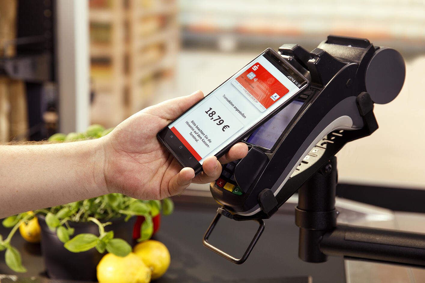 eine Person hält ein Smartphone mit eingeblendeter Sparkassenkarte vor ein Lesegerät