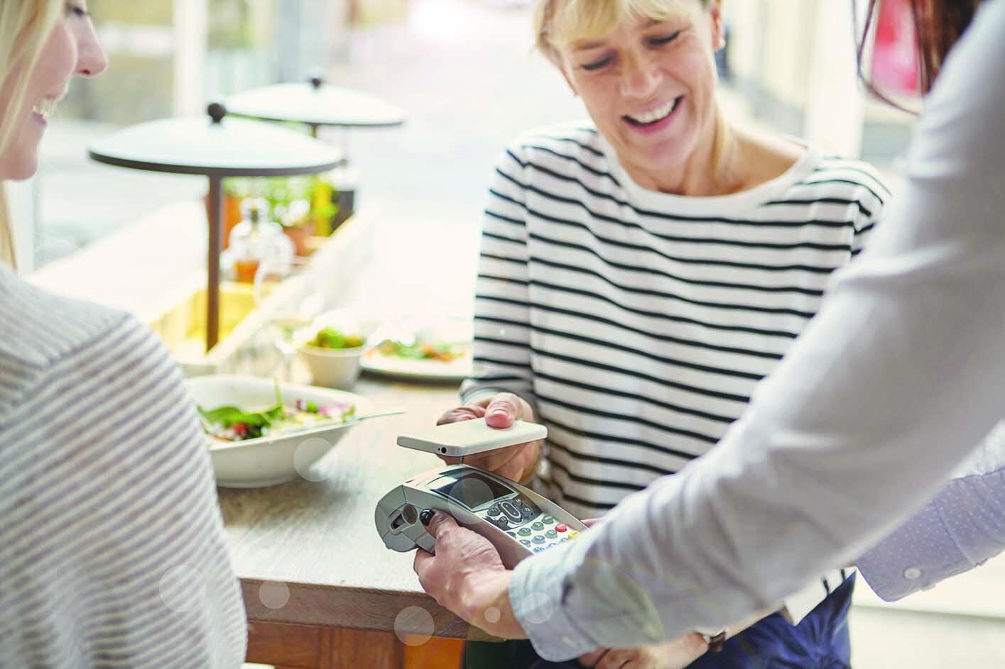 eine Frau beim mobilen Bezahlen mit Smartphone in einem Bistro