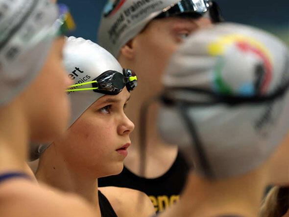 Gruppe junger Schwimmerinnen mit Badekappen und Chlorbrillen.